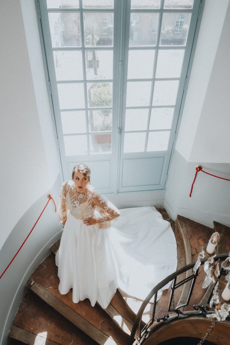 Une mariée rayonnante sur l'escalier courbe de Dax Meysonnave, baignée par la lumière naturelle des Landes authentiques.