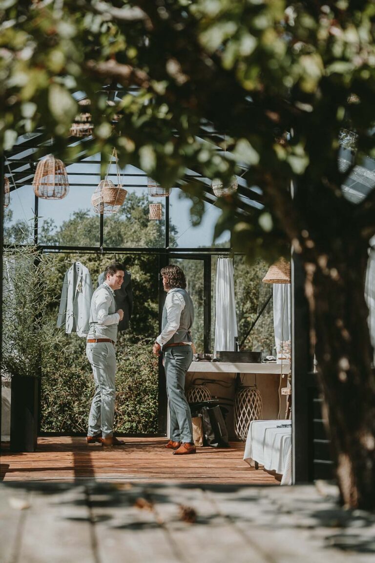 Deux hommes élégants échangent dans une verrière baignée de lumière, ambiance intime et végétale, idéale pour photo mariage Landes.