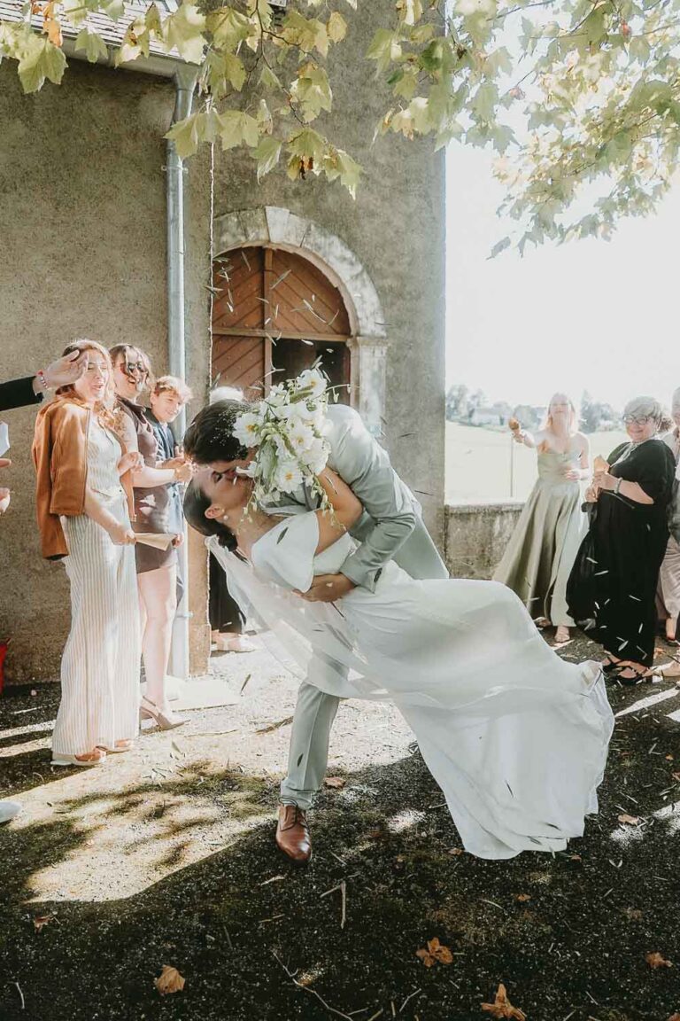 Un couple de jeunes mariés s'embrasse tendrement, entouré de proches sous les arbres, ambiance douce des Landes.