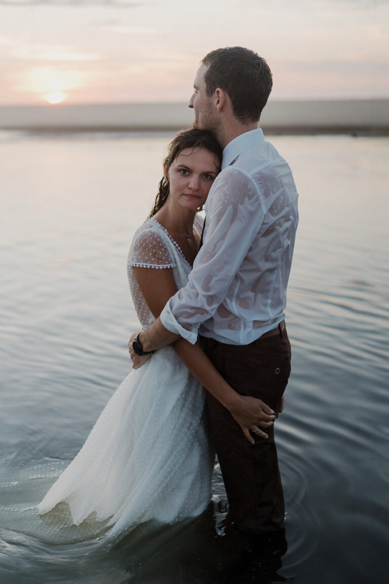 Dans les Landes, un couple s'enlace tendrement au coucher du soleil dans l'eau, ambiance douce et naturelle pour souvenirs précieux.