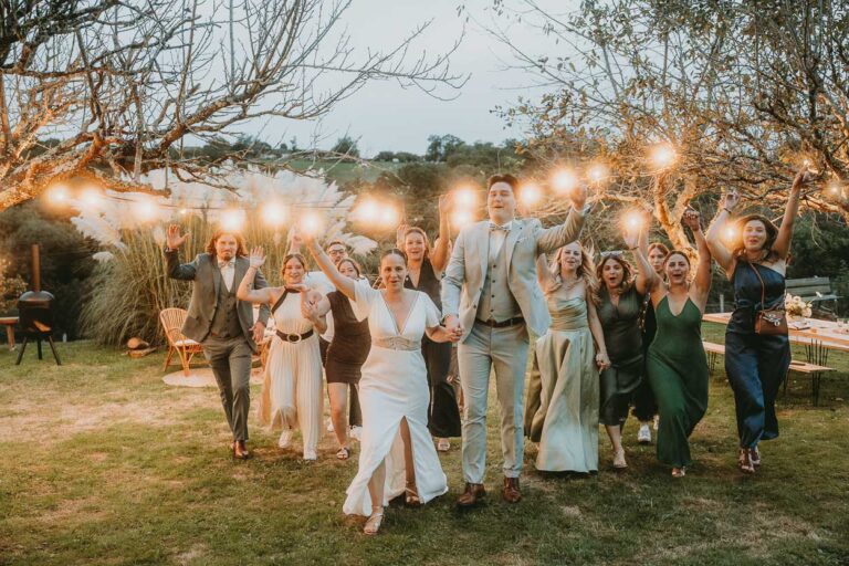 Moment complice des mariés main dans la main, entourés d'invités sous guirlandes, ambiance douce d'un mariage Landes.