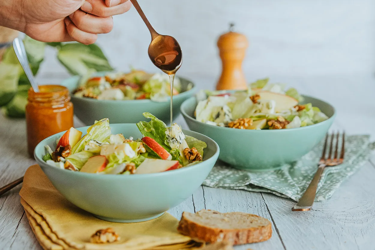 Dans une ambiance conviviale à Dax, une main verse la sauce sur une salade partagée lors d'un repas familial chaleureux.