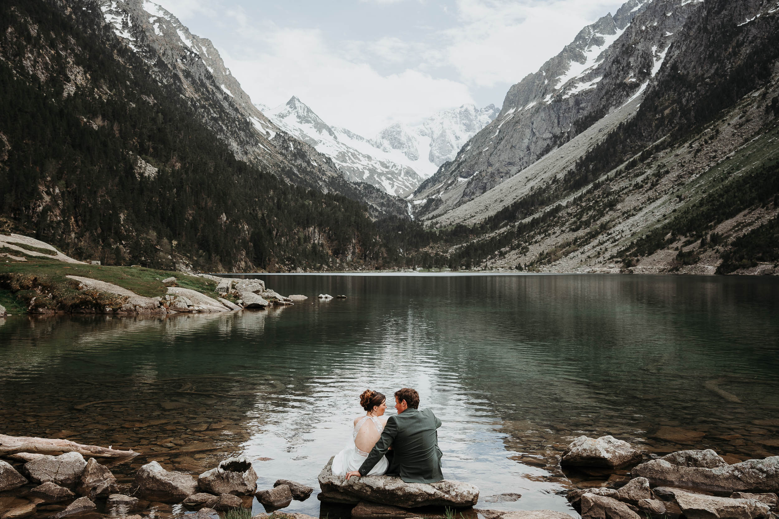 Deux amoureux assis au bord d'un lac alpin, montagnes en toile de fond, douceur et complicité lors d'une séance photo couple.