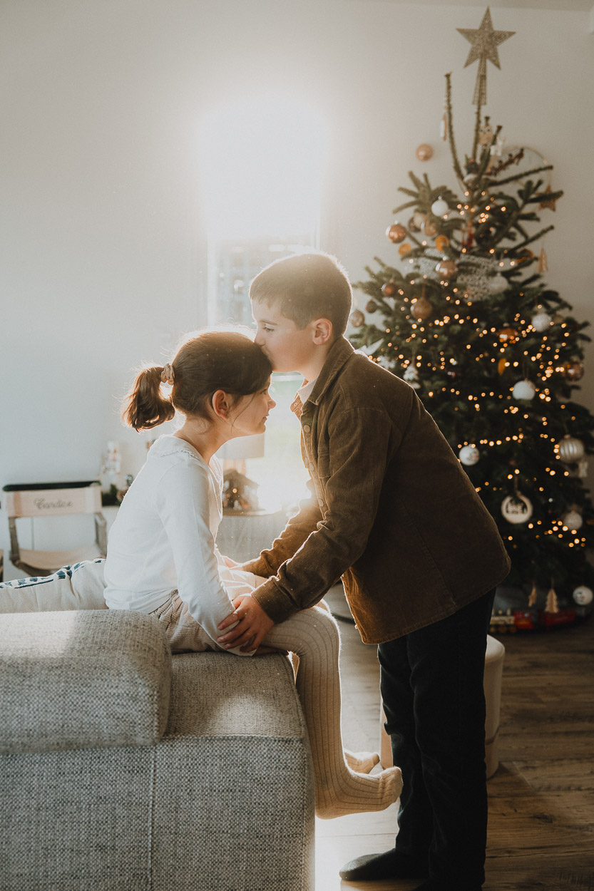 Tendresse d'un jeune couple près du sapin, instant magique capturé dans un salon landais par Photographe Dax.