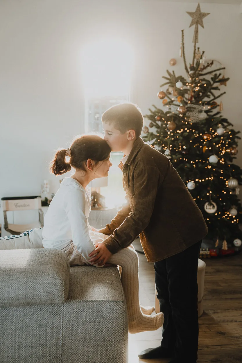 Tendresse d'un jeune couple près du sapin, instant magique capturé dans un salon landais par Photographe Dax.