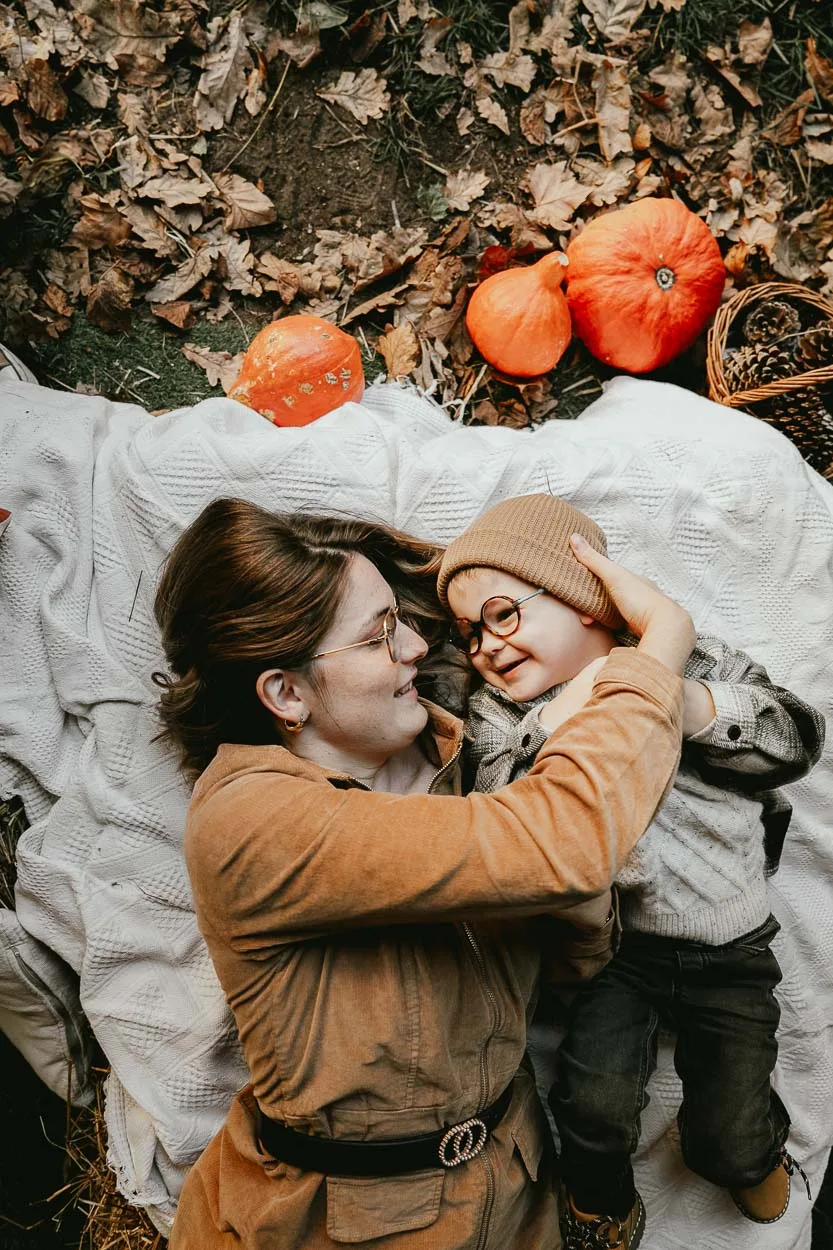 Un doux moment mère-enfant sur une couverture, entourées de feuilles d'automne et citrouilles dans les Landes.