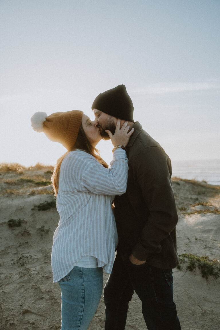 Un couple s'embrasse tendrement sur une dune des Landes, capturé sous le ciel limpide près de Dax, ambiance naturelle et intime.