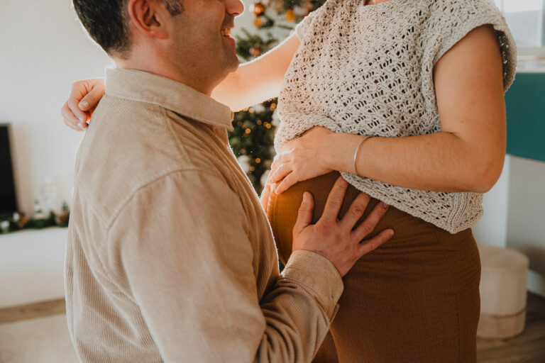 Un futur papa touche tendrement le ventre de sa compagne, dans une lumière douce, près de Dax au cœur des Landes.