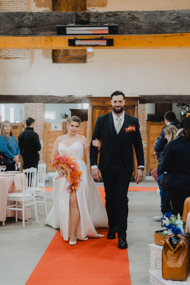 Un doux moment de mariage dans les Landes : les mariés avançant sur un tapis rouge, sourire aux lèvres, entourés de proches.