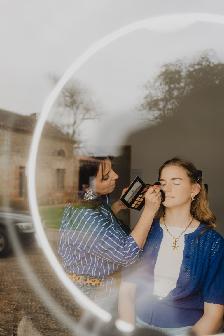 Une future mariée se prépare en douceur, maquillée dehors, reflet tendre dans un miroir rond, ambiance Landes intimiste.