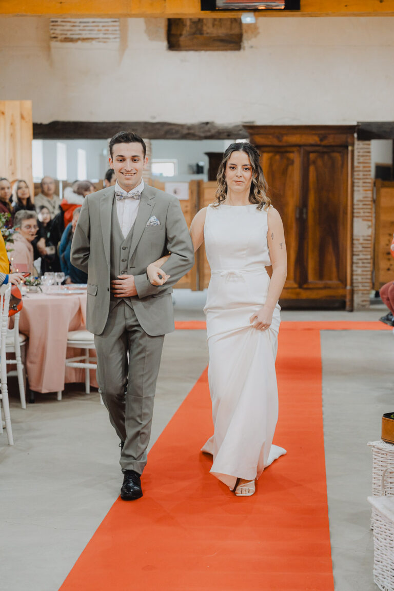 Un couple lumineux avance main dans la main sur le tapis rouge, ambiance élégante captée lors d'un mariage raffiné dans les Landes.