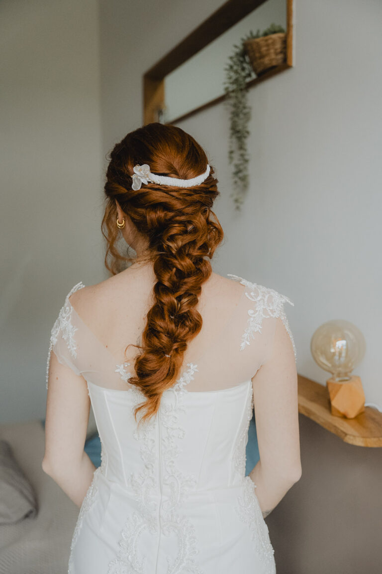 Votre belle chevelure rousse tressée, parée d'ornements, illumine la robe dentelle dans une ambiance douce des Landes.