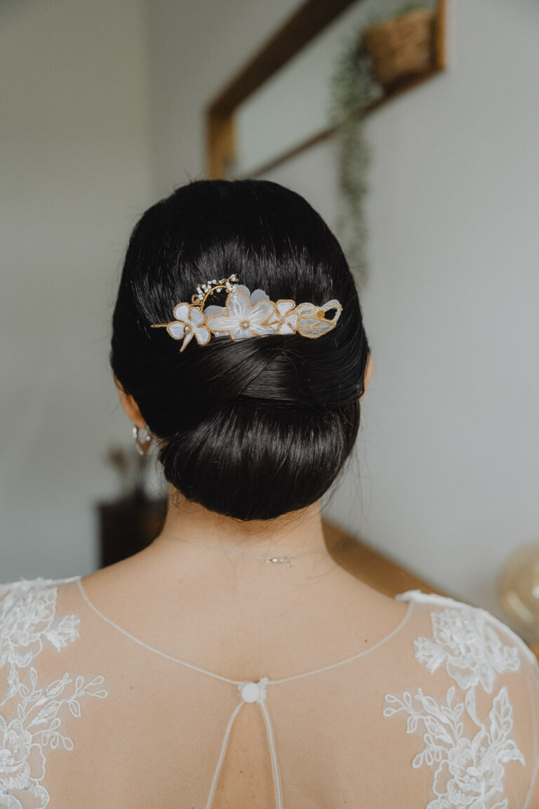 Une jeune femme coiffée d'un chignon bas orné de fleurs, en robe dentelle, capte l'élégance et la douceur d'un mariage dans les Landes.