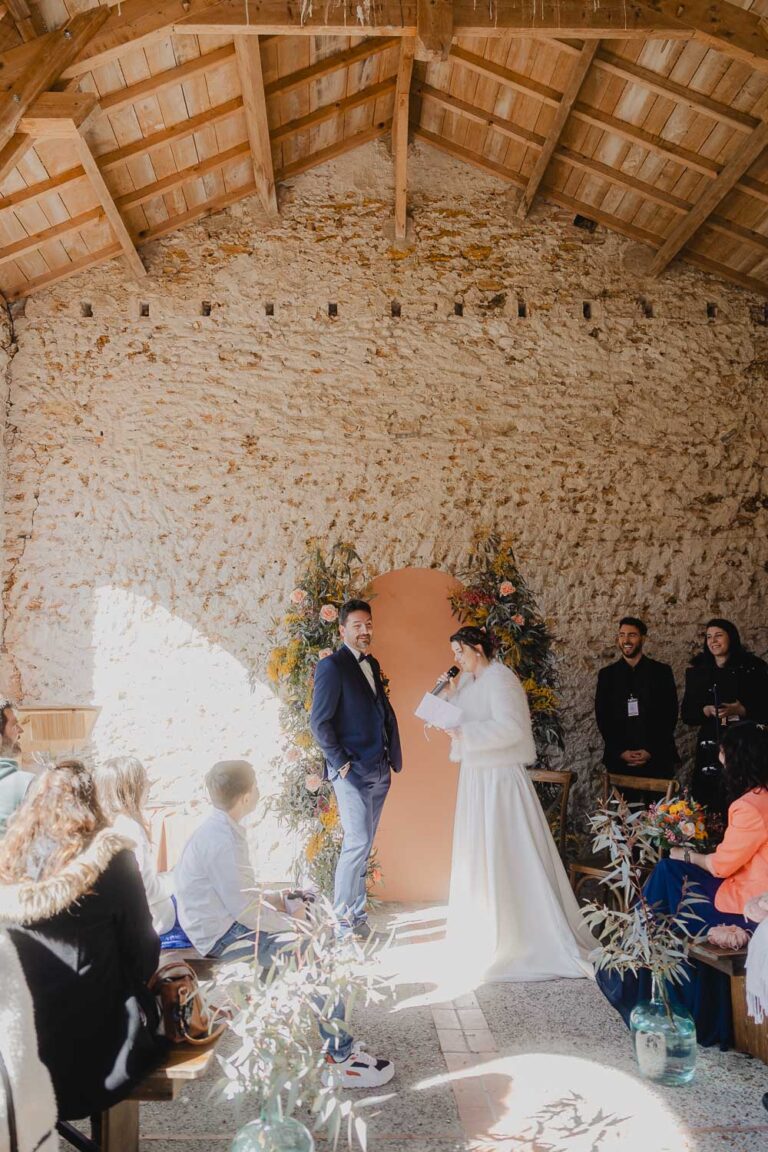 Dans une salle lumineuse, deux amoureux échangent un regard tendre, entourés des proches et de fleurs, capturés dans les Landes.