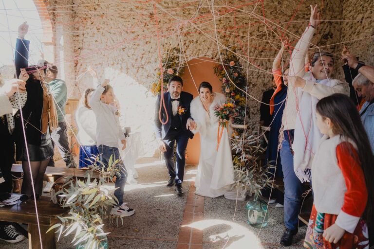 Un couple radieux franchit une arche en pierre, entouré de rubans festifs, dans l'ambiance joyeuse d'un mariage familial dans les Landes.