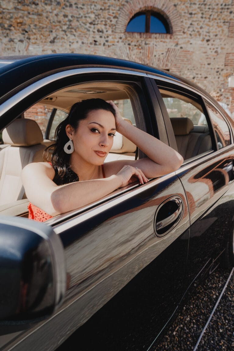 Une femme détendue à la portière d'une voiture noire, sourire discret, lumière douce, ambiance authentique façon Landes.