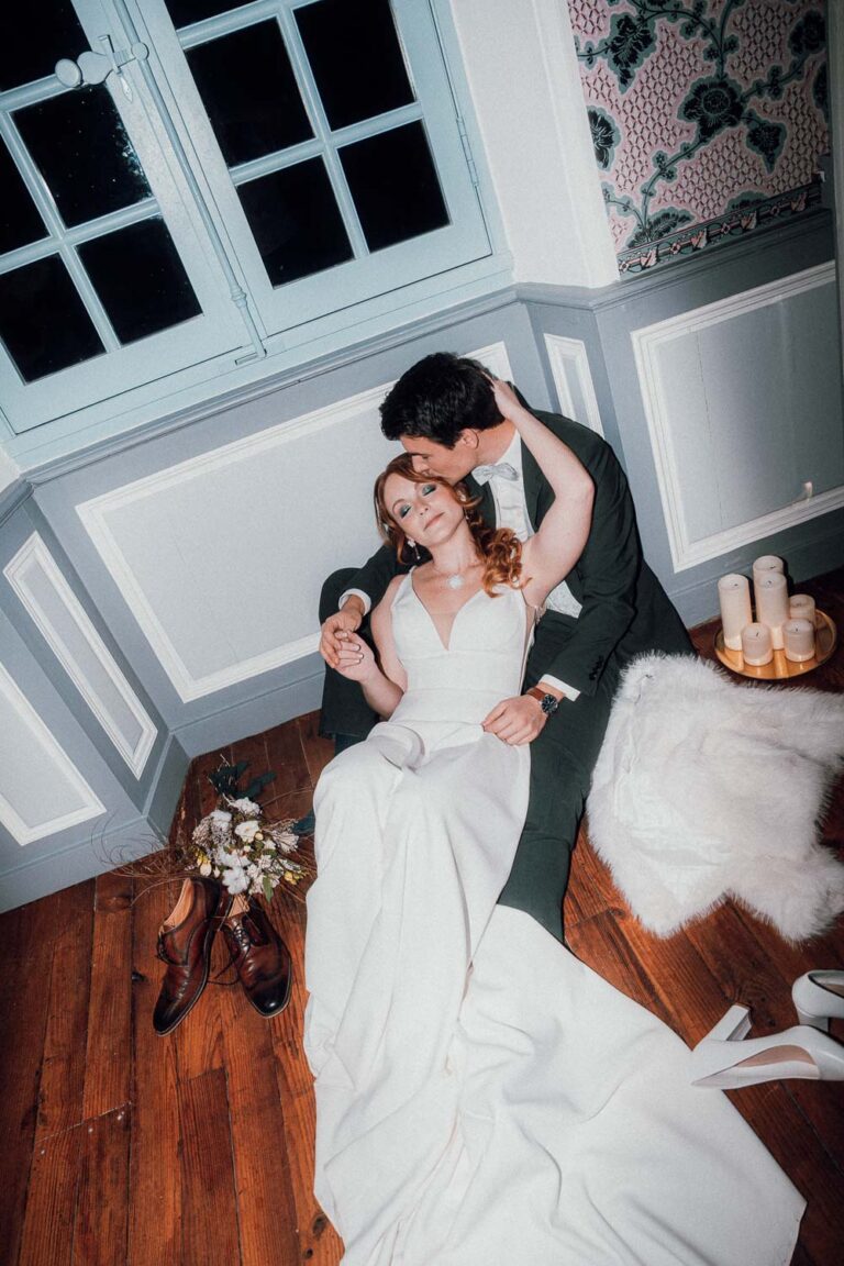 Instant complice : mariés tendres assis au sol, bouquet et bougies créent une ambiance douce typique d'un mariage dans les Landes.