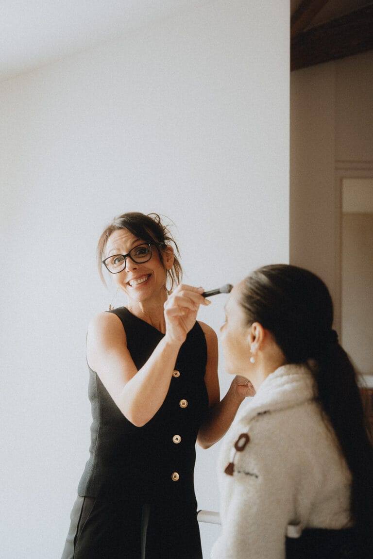 Moment complice lors d'une séance famille à Dax : maquillage et rires entre femmes dans un salon baigné de lumière.