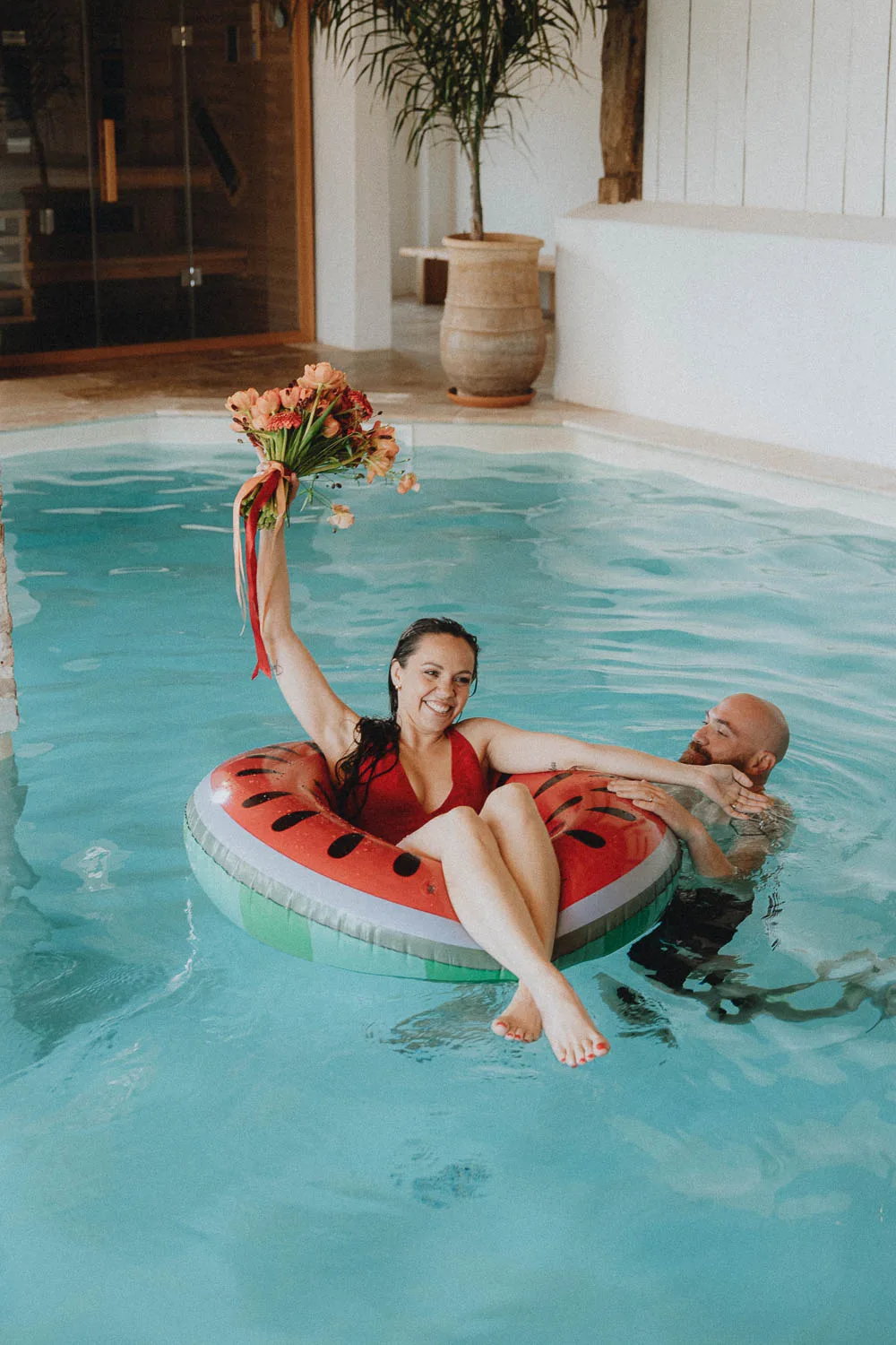 Sourires complices à la piscine couverte de Dax : séance en famille dans les Landes, sur une bouée en forme de pastèque, un bouquet à la main.