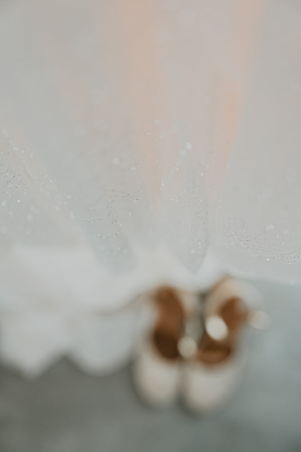 La douceur d’un mariage à Dax : un tissu blanc scintillant, des chaussures dorées qui se fondent dans le sol gris, un détail raffiné.