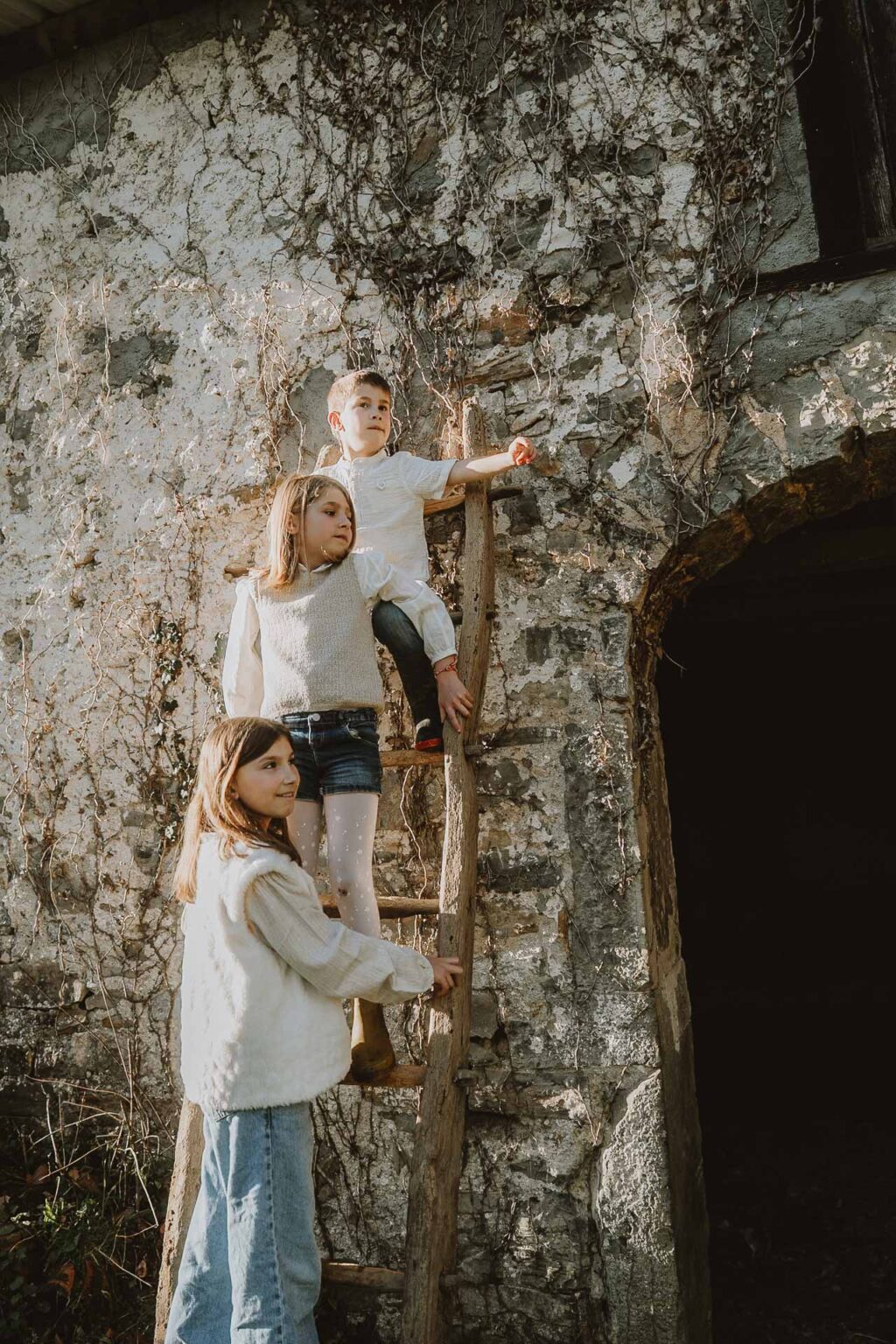 Des enfants qui rient sur une échelle en bois adossée à un mur ancien à Dax, des moments de complicité lors d’une séance photo en famille.