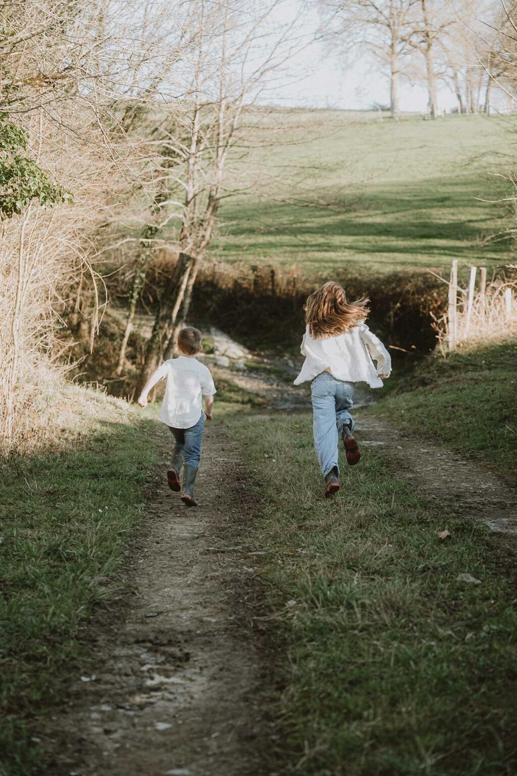 Des enfants rieurs courant sur un sentier ensoleillé, séance photo en famille dans la nature à Dax, dans les Landes, par Allison Micallef.