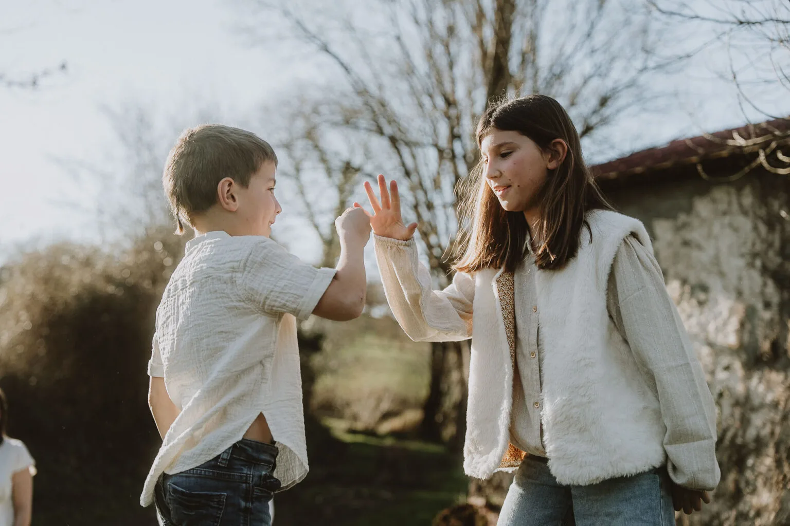 Des enfants rient en se tapant dans la main sous le soleil, dans un jardin des Landes ; séance photo en famille à Dax par Allison Micallef.