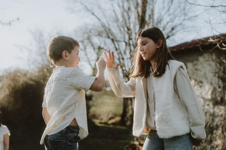 Des enfants rient en se tapant dans la main sous le soleil, dans un jardin des Landes ; séance photo en famille à Dax par Allison Micallef.