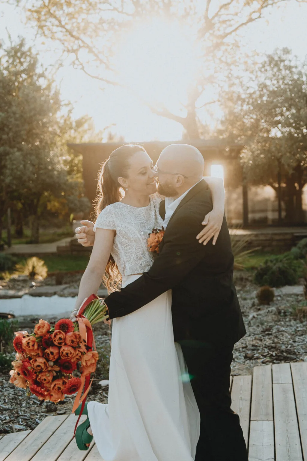 La tendresse d’un couple marié s’embrassant au coucher du soleil à Dax, bouquet aux teintes orangées.
