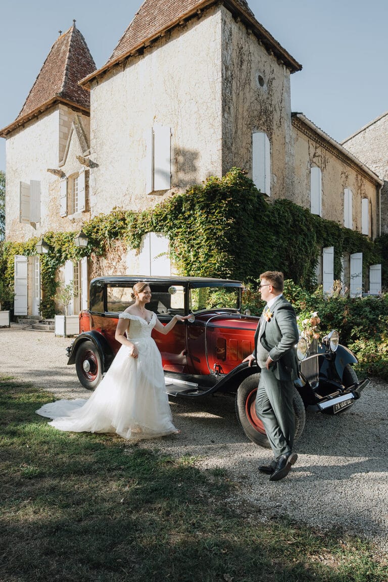 Des jeunes mariés complices devant une voiture ancienne et un château à Dax, dans les Landes.