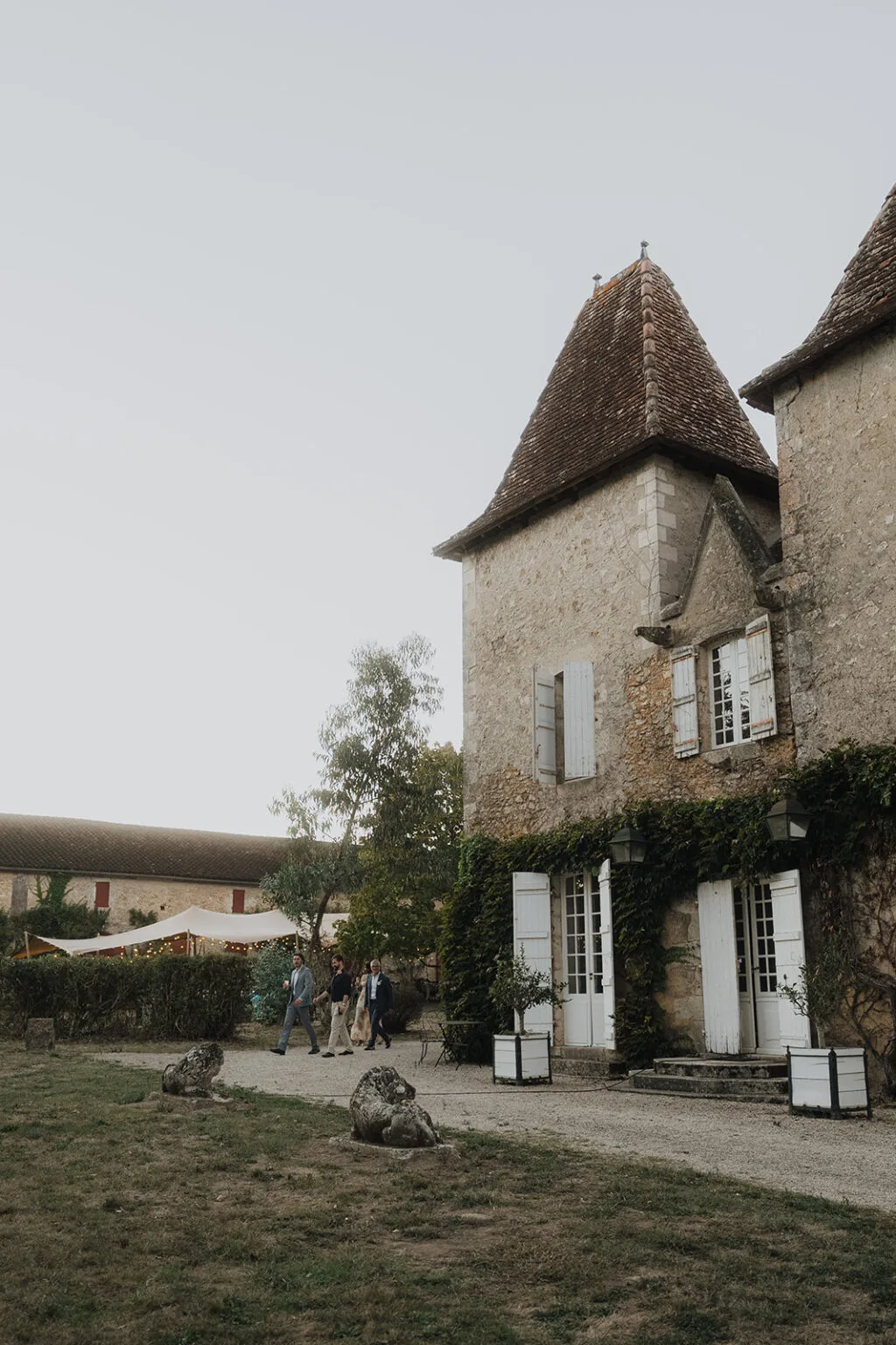 Des invités traversant le jardin d'un domaine en pierre pour se rendre à un mariage dans les Landes.