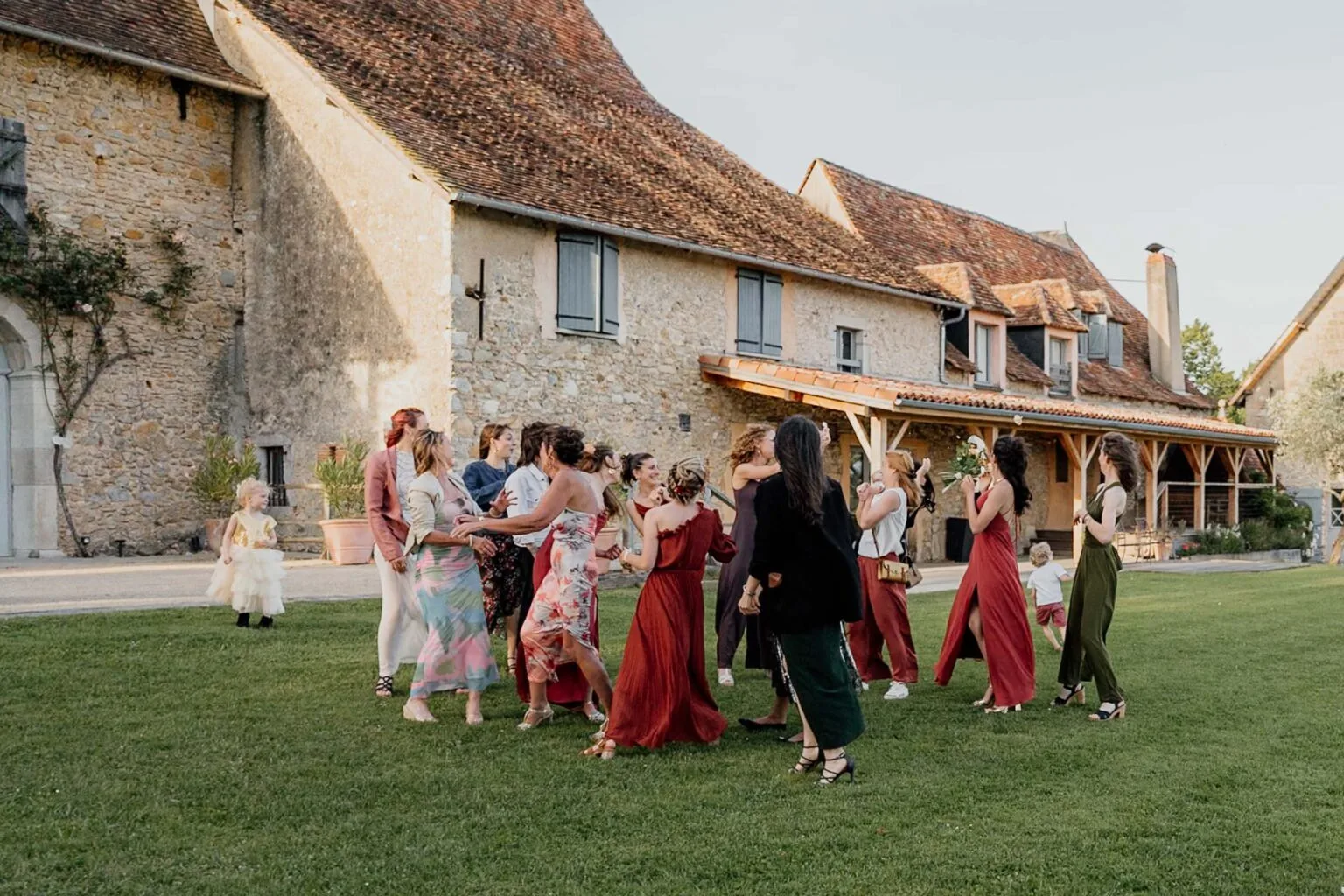 Des invités en fête dansant devant une ferme en pierre, mariage photographié par Allison Micallef, dans les Landes.