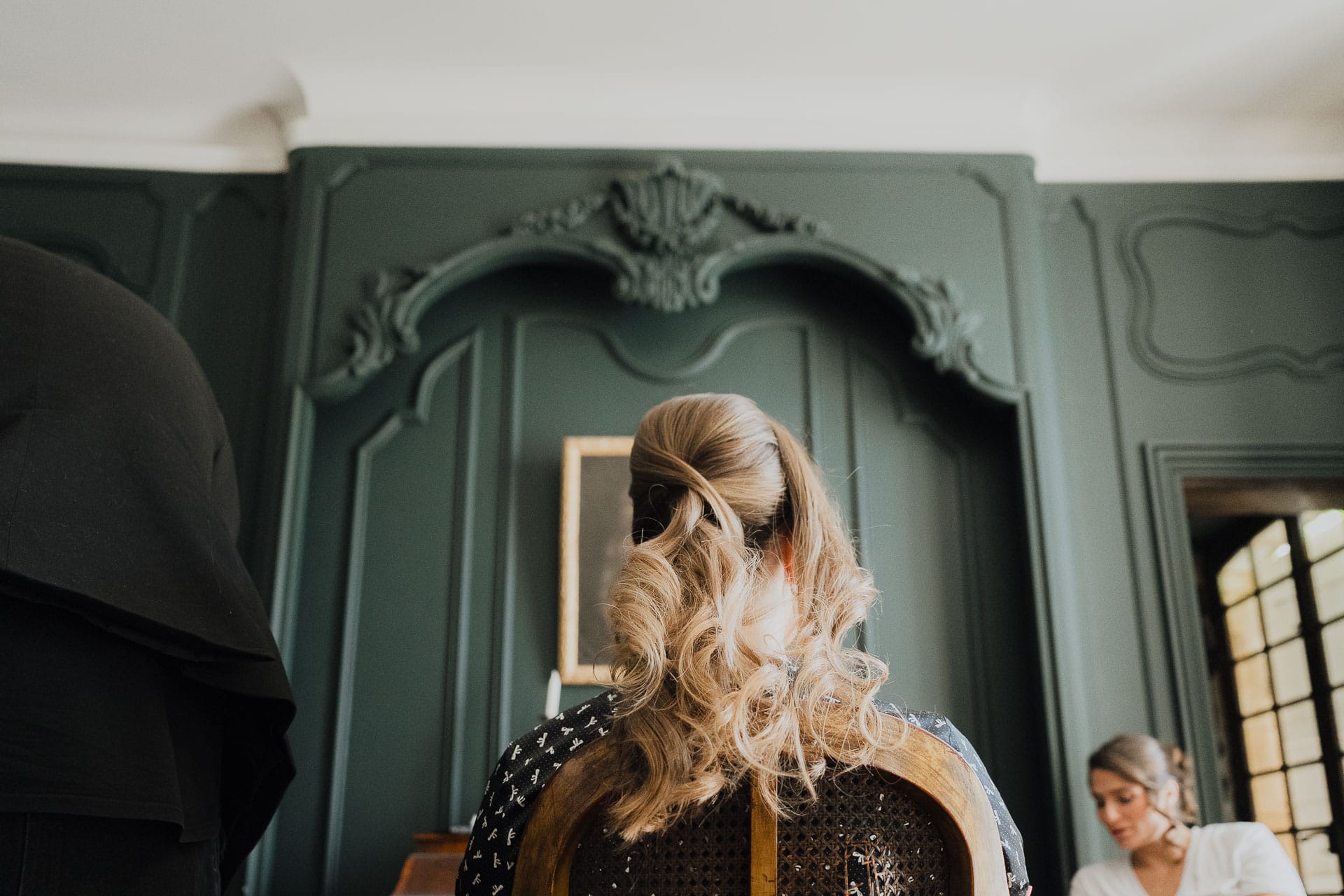 Coiffure de la mariée devant une glace ancienne, dans une pièce aux murs vert sombre