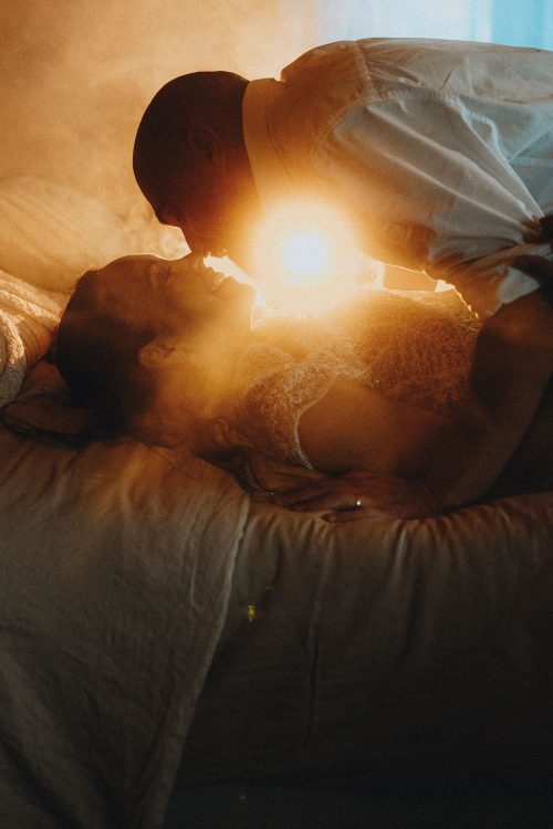 Tendresse d'un couple allongé sur un lit, lumière douce à Dax, séance photo intimiste par Allison Micallef.