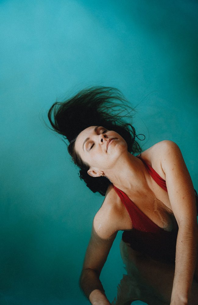 Joie d'une femme en maillot rouge, cheveux flottant dans l'eau bleue, séance famille à Dax avec Allison Micallef.