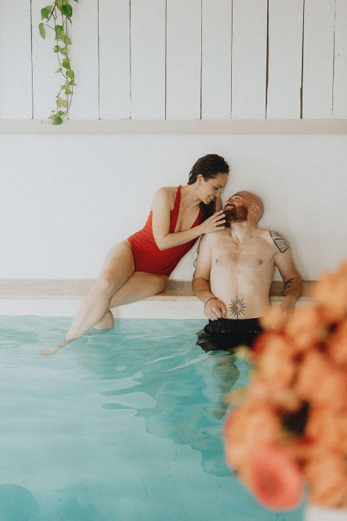 Tendresse au bord d'une piscine à Dax : complicité d'un couple enlacé, fleurs en douceur au premier plan.