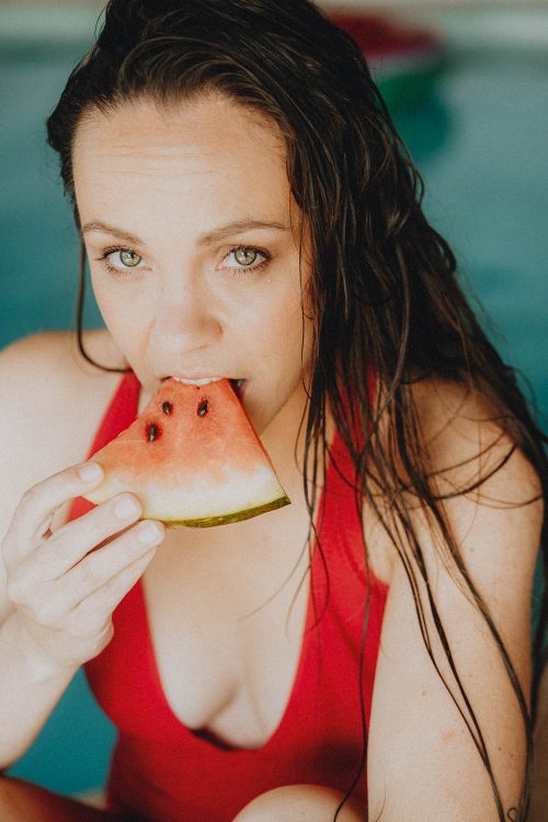 Joie estivale d'une jeune femme savourant une pastèque au bord d'une piscine à Dax, séance famille Landes.