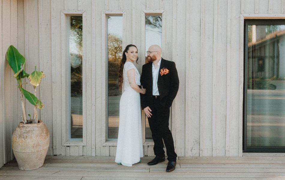 Couple complice souriant devant une bâtisse en bois à Dax, Landes, séance photo mariage naturelle et chaleureuse.
