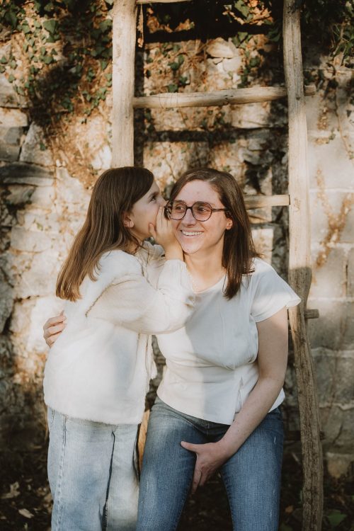 Une complicité mère-fille lors d’une séance photo en famille à Dax, des éclats de rire devant un mur de pierre et une vieille échelle.