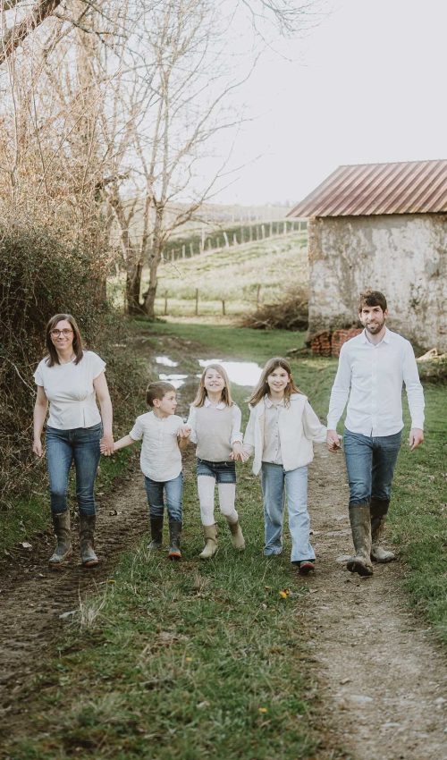 Sourires complices d'une famille se tenant la main sur un chemin de campagne, séance photo à Dax, dans les Landes.