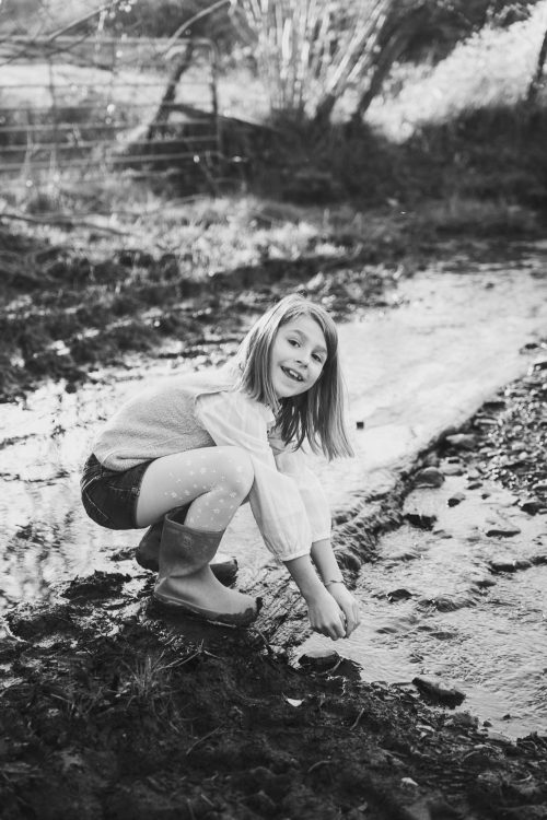 Une petite fille joyeuse explore un ruisseau à Saint-Paul-lès-Dax, séance photo en famille dans les Landes avec Allison Micallef.