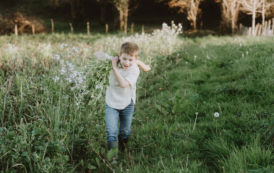 Un petit garçon joyeux, vêtu d'un jean et d'une chemise blanche, traverse un champ fleuri à Dax lors d'une séance photo familiale pleine de chaleur.