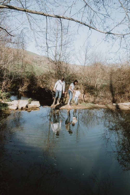 Une famille traversant un ruisseau en marchant sur des pierres à Dax, dans les Landes : un moment de complicité immortalisé lors d’une séance photo en famille.