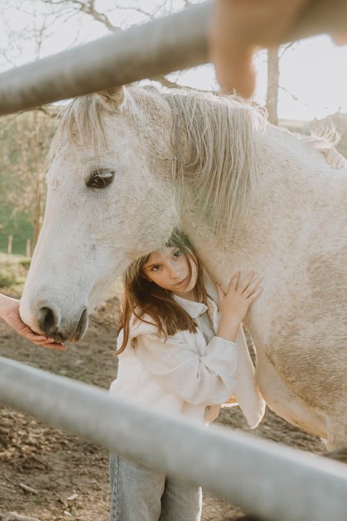 Un moment de complicité entre une petite fille et son cheval près d’une clôture, sous une lumière douce à Dax, lors d’une séance photo en famille dans les Landes.