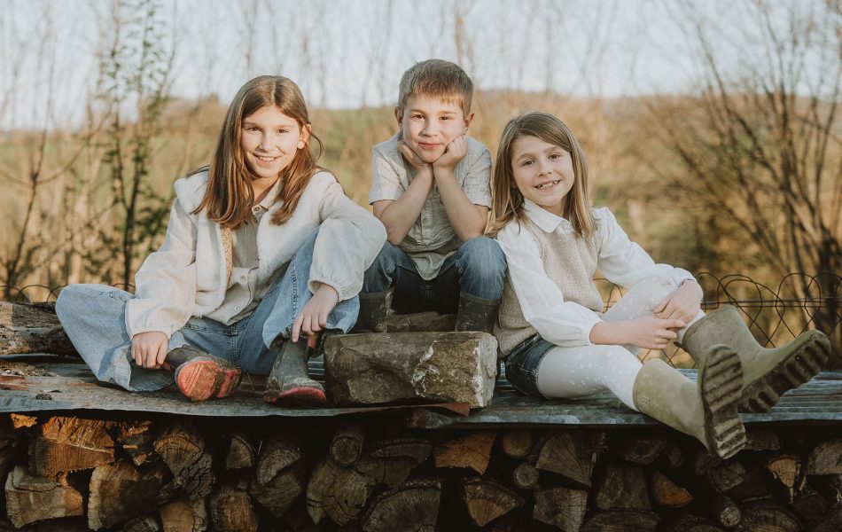 Rires d'enfants assis sur des bûches dans la forêt près de Dax, séance photo de famille dans les Landes, empreinte de complicité.
