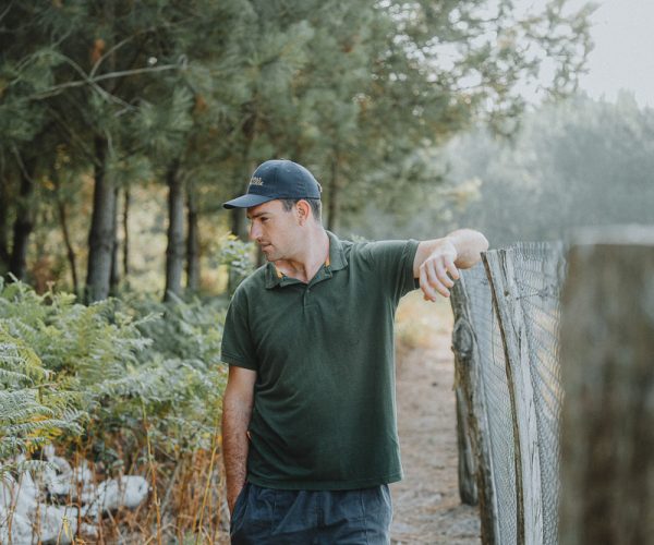 Un homme pensif près d'une barrière en bois, entouré de verdure, ambiance douce et naturelle dans les Landes.