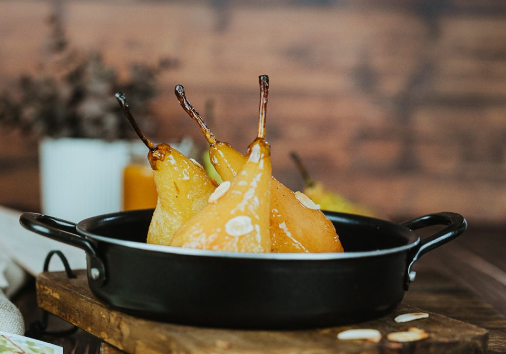 Dans une lumière douce, trois poires pochées reposent sur un plat sombre, ambiance chaleureuse comme lors d'un repas en famille.