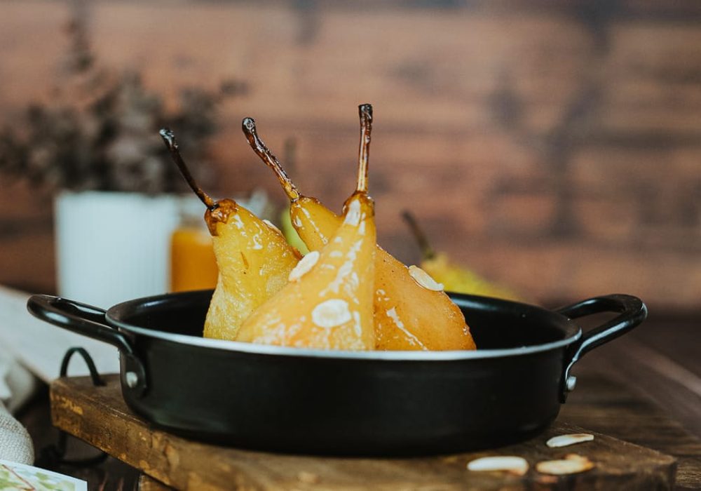 Dans une lumière douce, trois poires pochées reposent sur un plat sombre, ambiance chaleureuse comme lors d'un repas en famille.