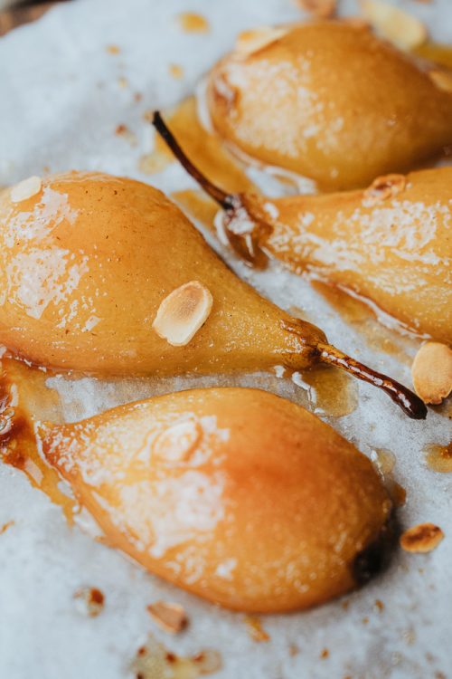 Quatre poires rôties dorées, nappées d'amandes, posées sur du papier cuisson, ambiance douce et conviviale des Landes.