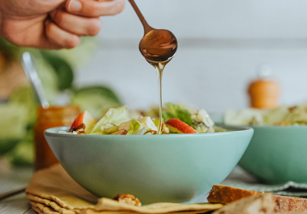 Un doux geste, du miel coule sur une salade verte, ambiance chaleureuse de repas familial dans une maison landaise.